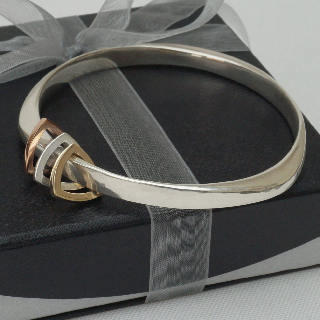 A silver heavy weight bangle bracelet with triangular charms, presented on a black box with a grey ribbon.