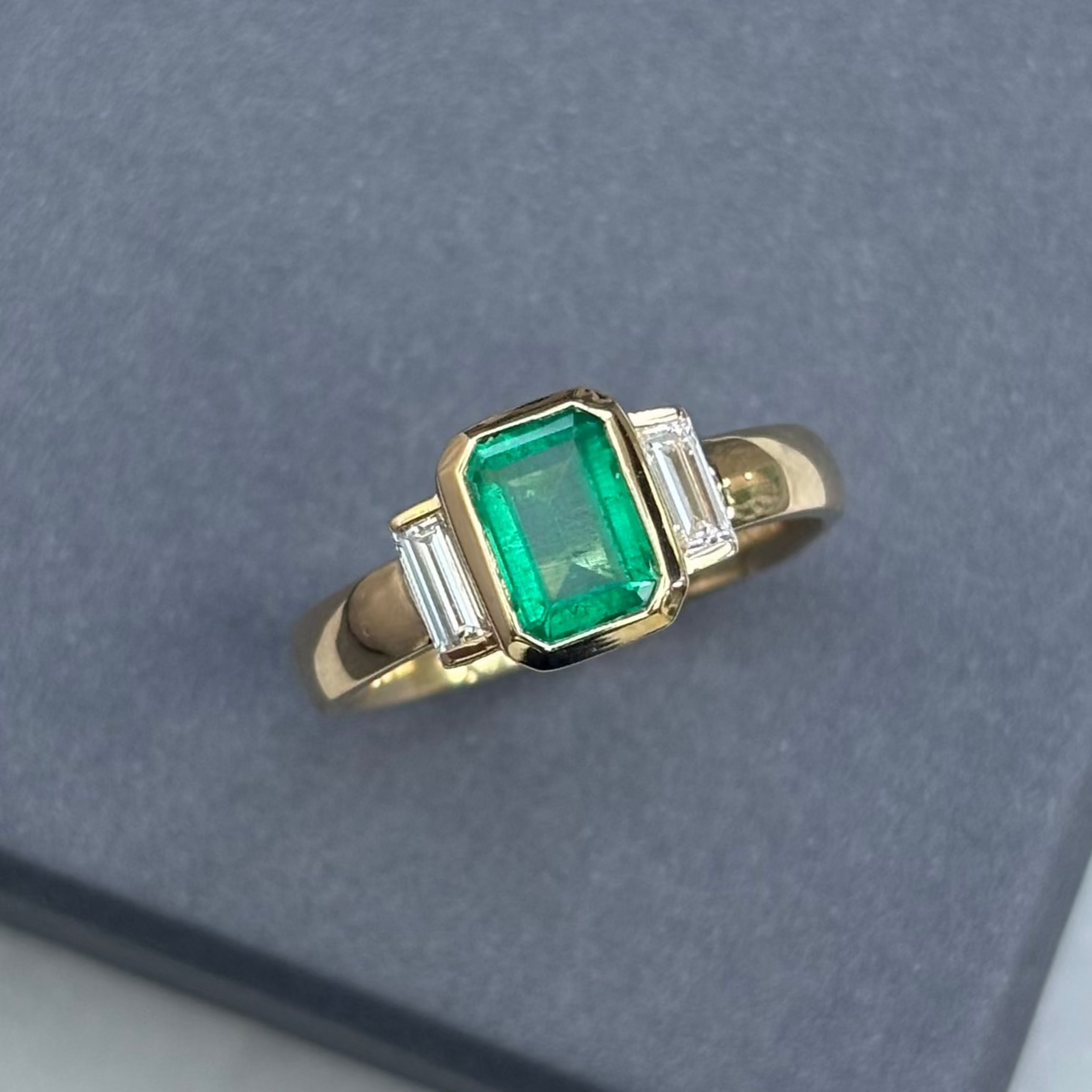 Gold  art deco ring with a emerald and smaller diamonds on a gray background