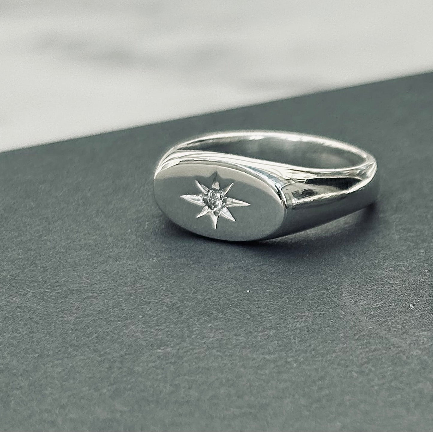 Silver signet ring with star set diamond design on a gray surface