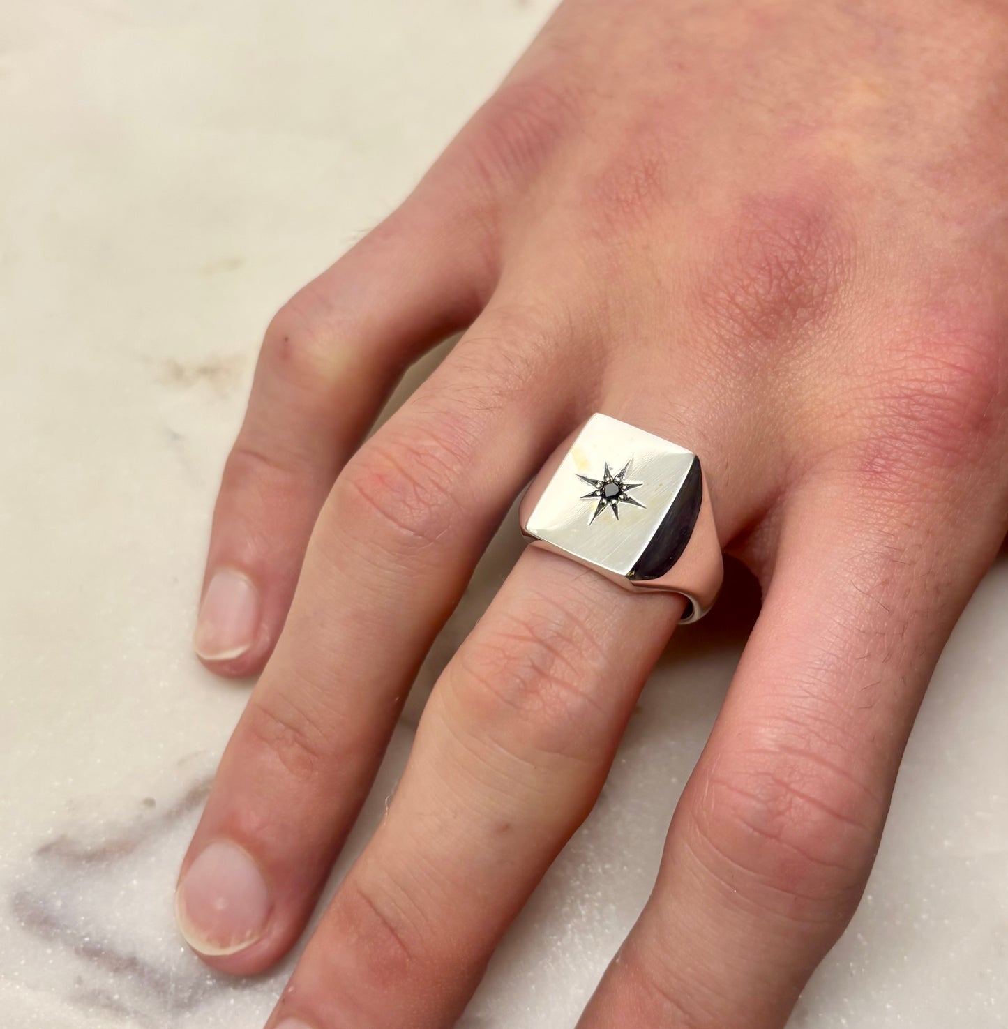 Hand wearing a silver signet  ring with a star design on a marble surface