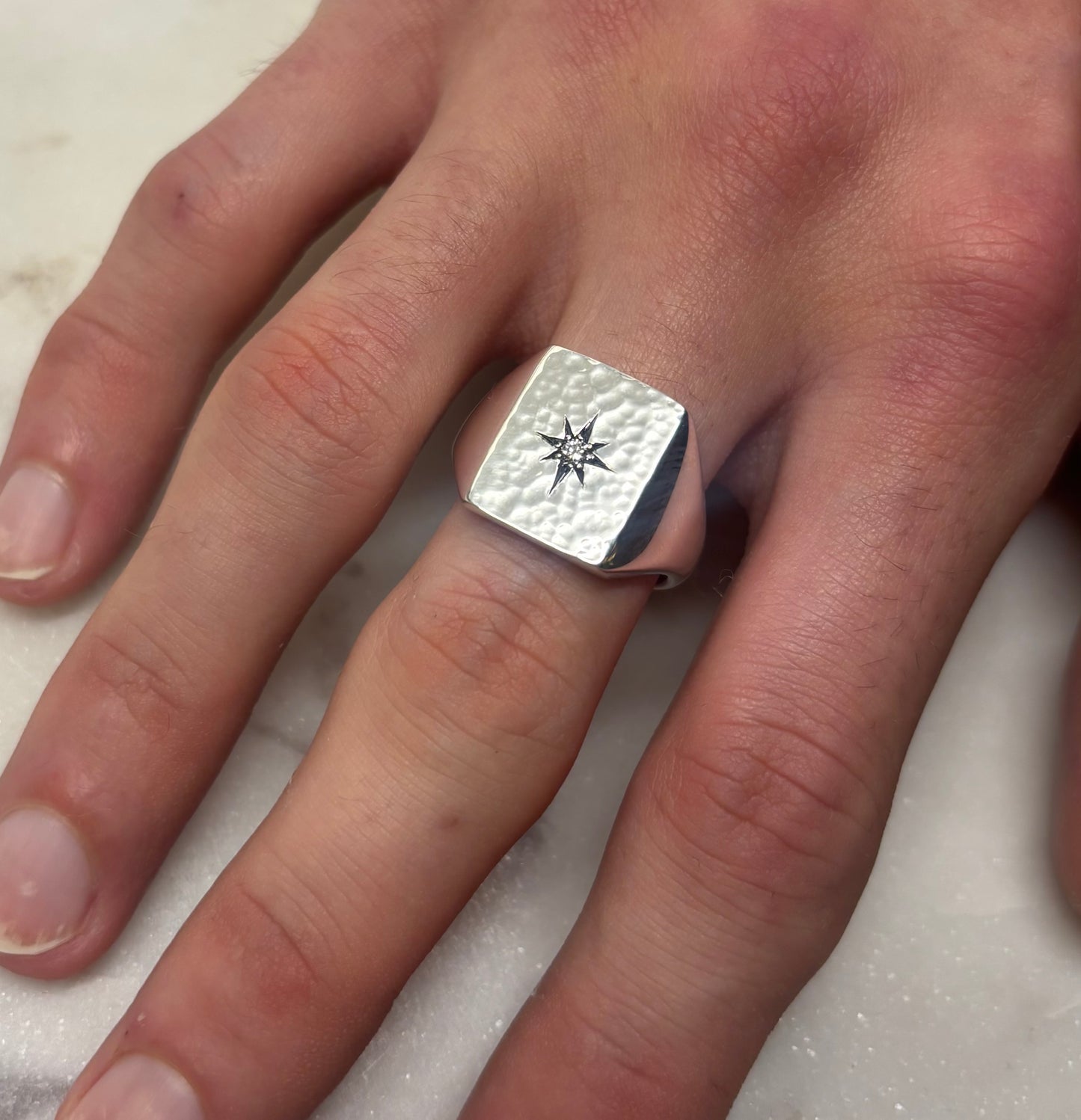 Silver ring with a star design on a person's finger against a neutral background