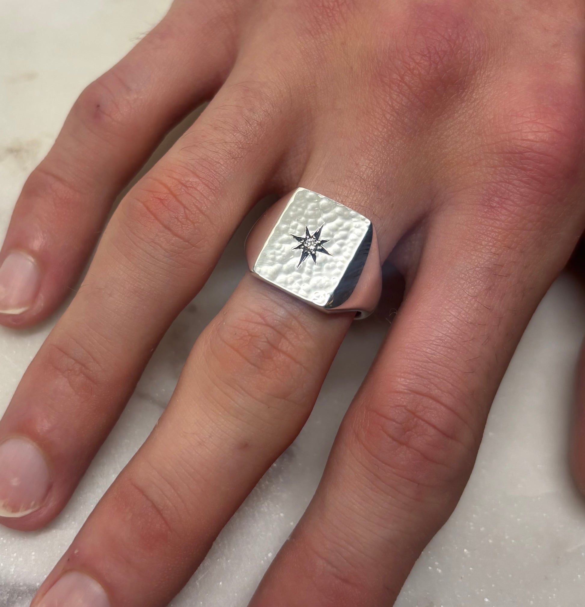 Silver ring with a star design on a person's finger against a neutral background