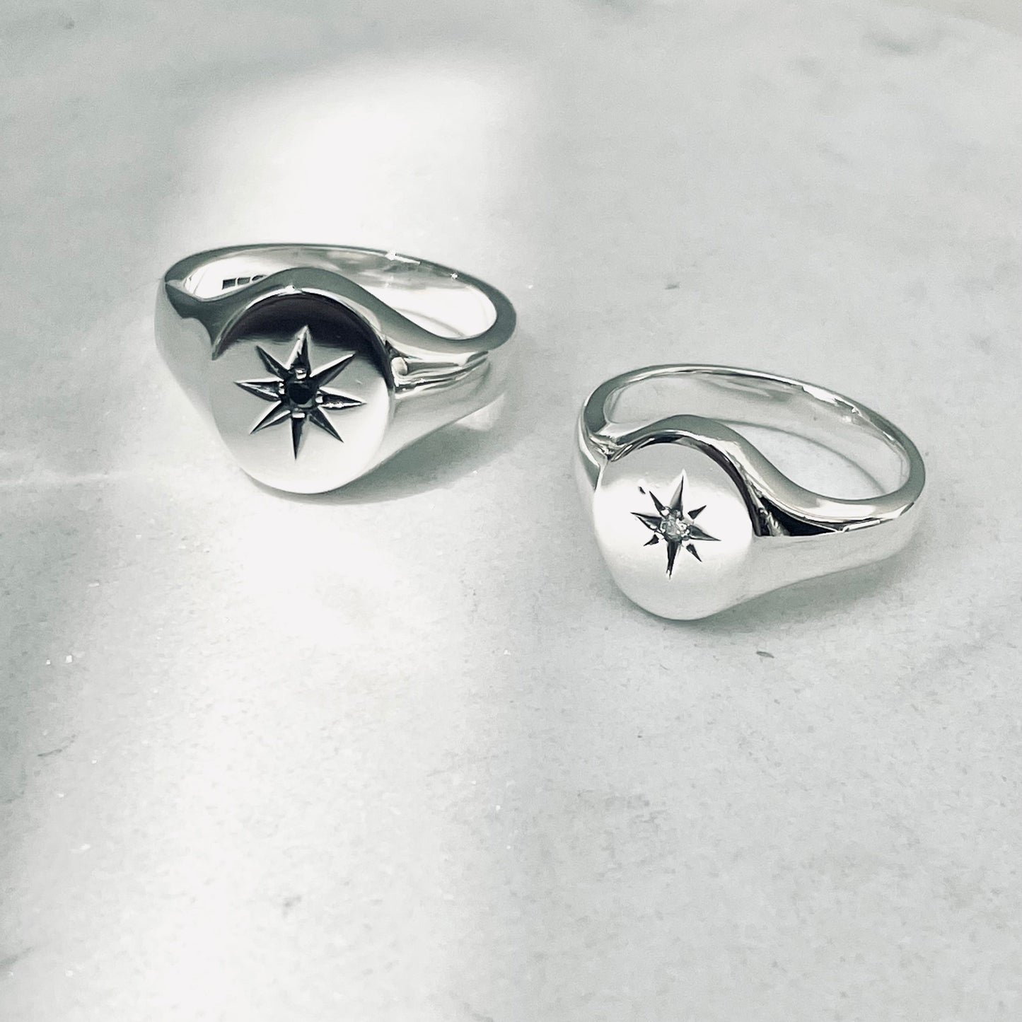 Two silver oval signet rings with star set diamond designs on a light gray background