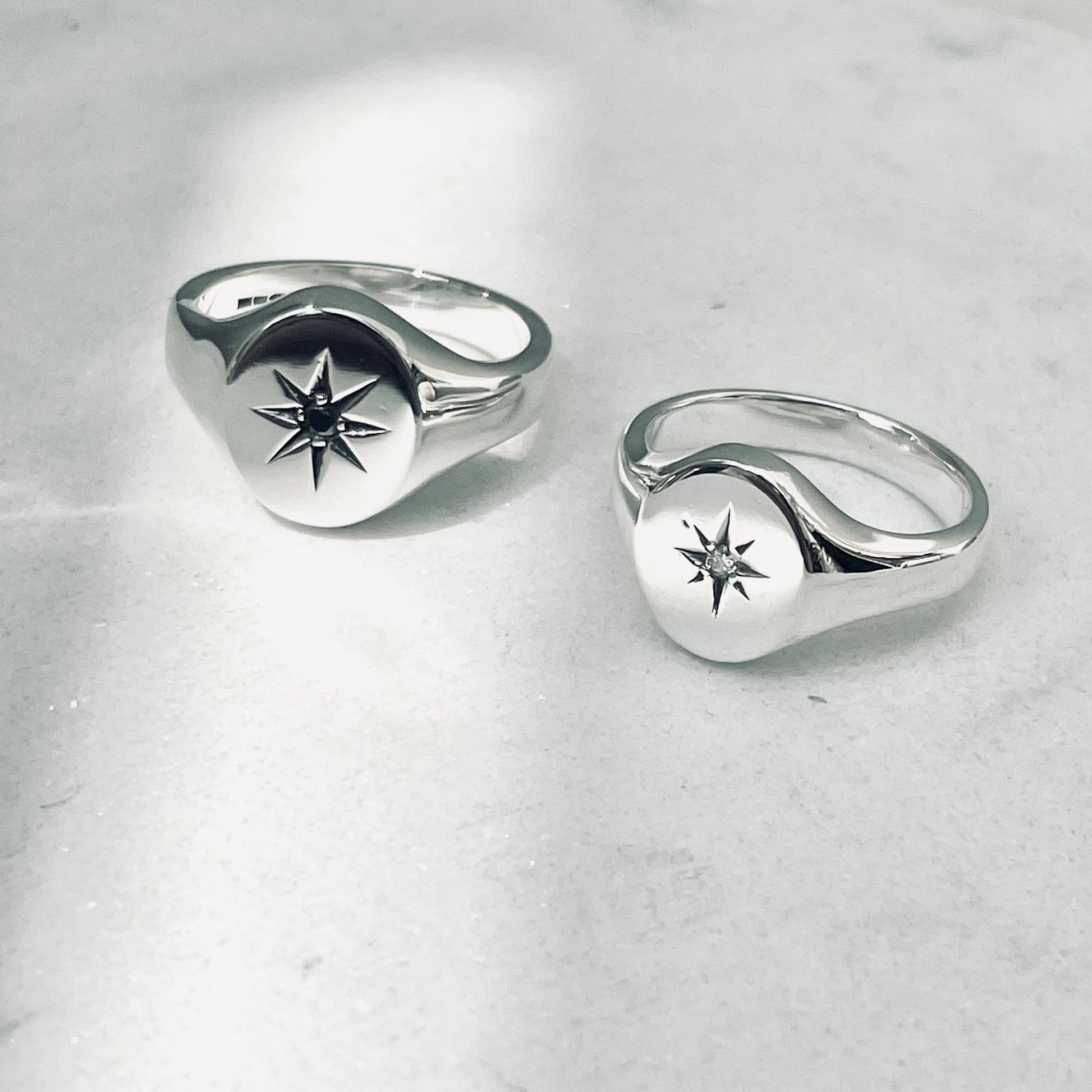 Two silver oval signet rings with star set diamond designs on a light gray background
