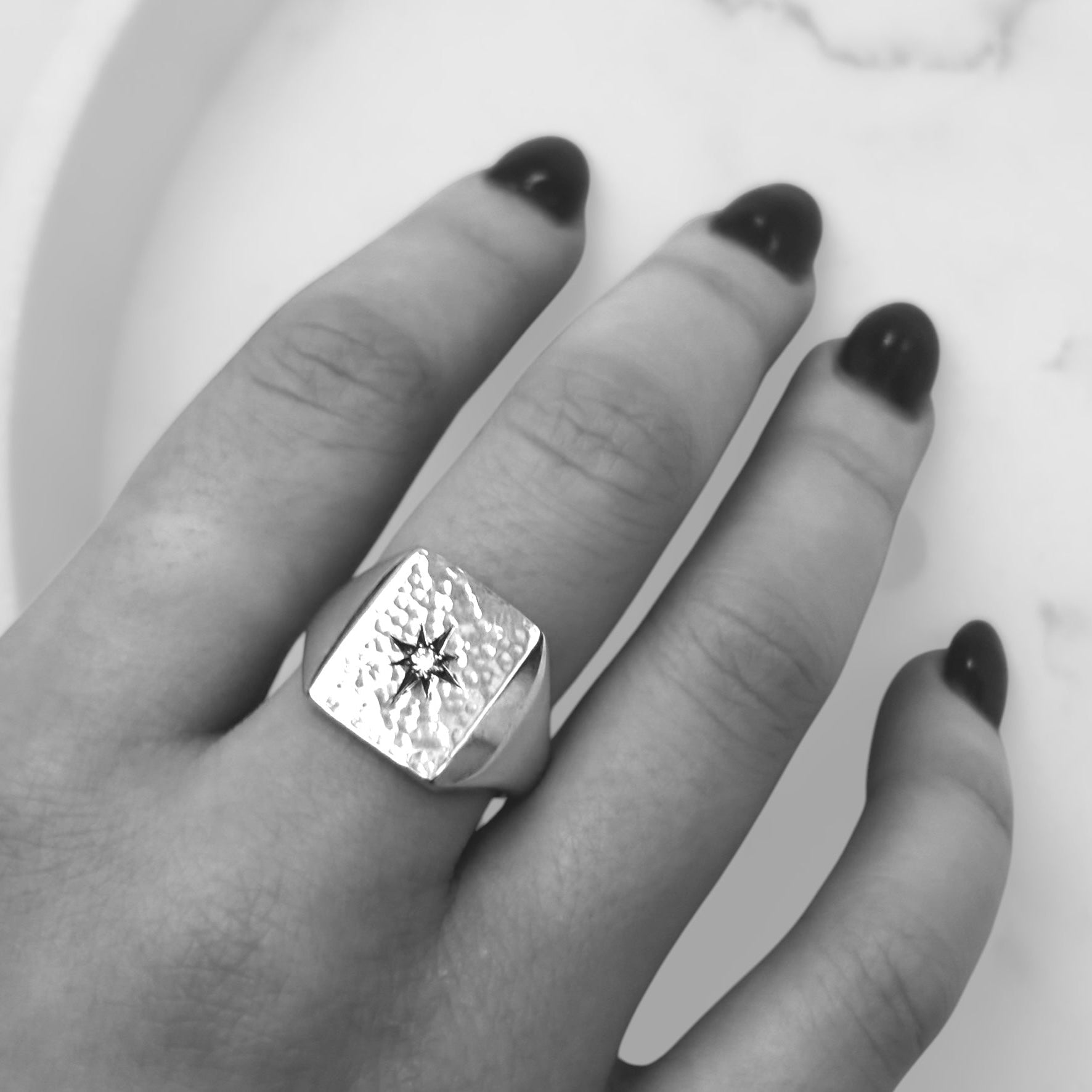 Hand wearing a large rectangular silver signet  ring with a star set diamond on a white background