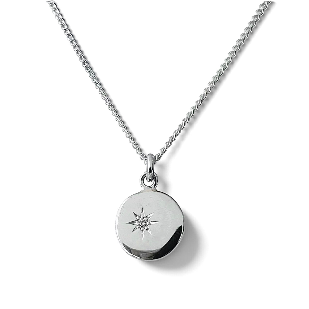A silver chain necklace with a round disc pendant featuring an engraved star design and a small diamond set in a starburst design, shown on a white background.
